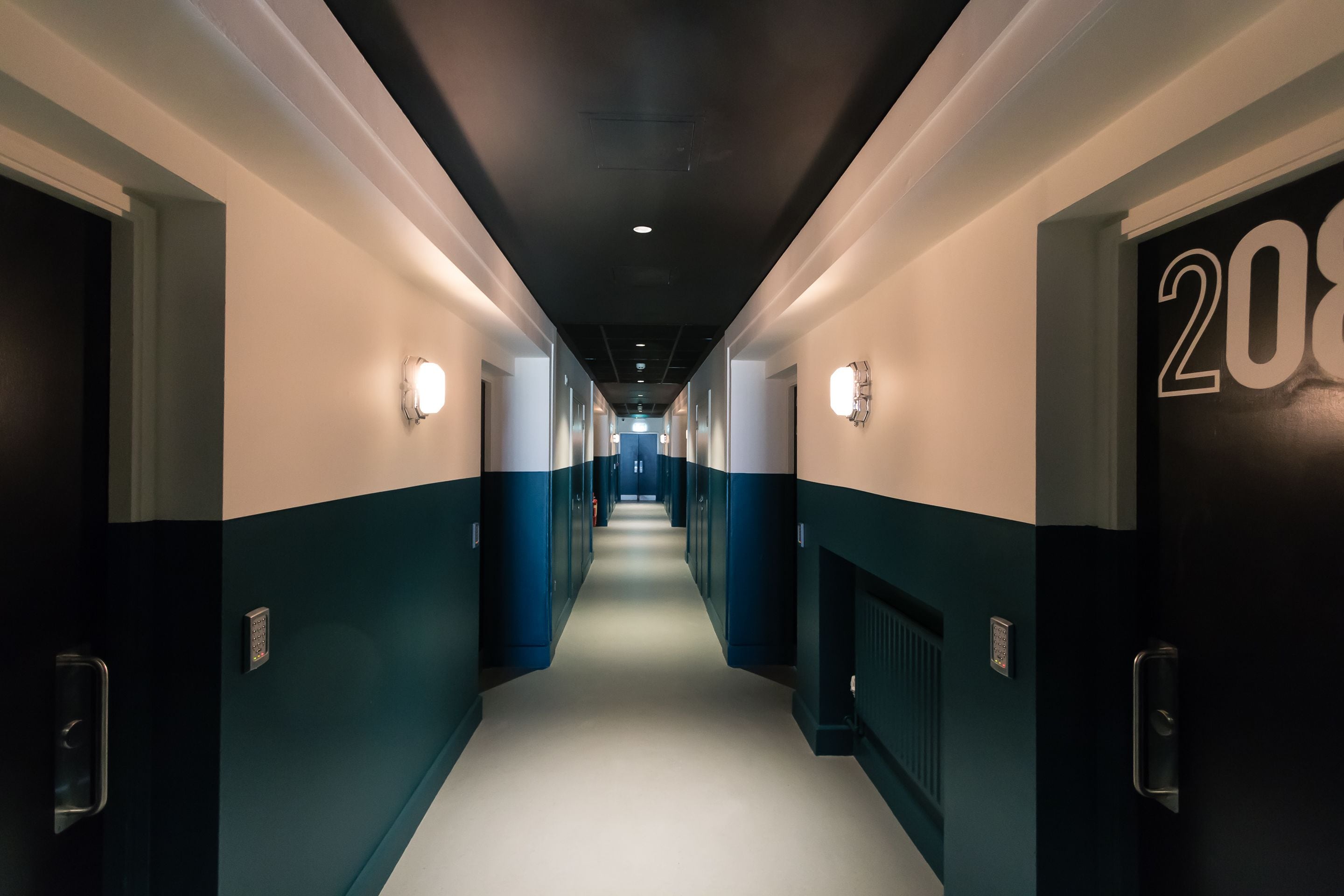 A hotel corridor with doors numbered 20 to 28, light fixtures on the walls, and a central light source at the end.