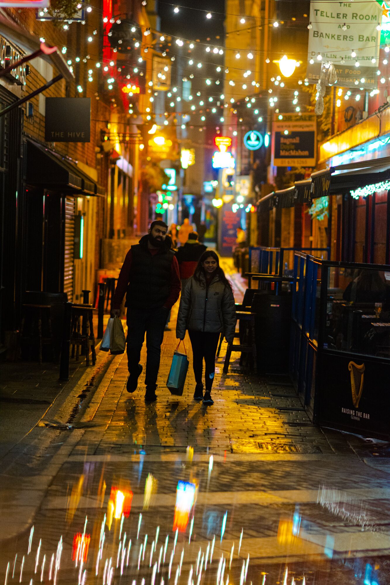A nighttime street scene with illuminated signs and a wet pavement reflecting lights.
