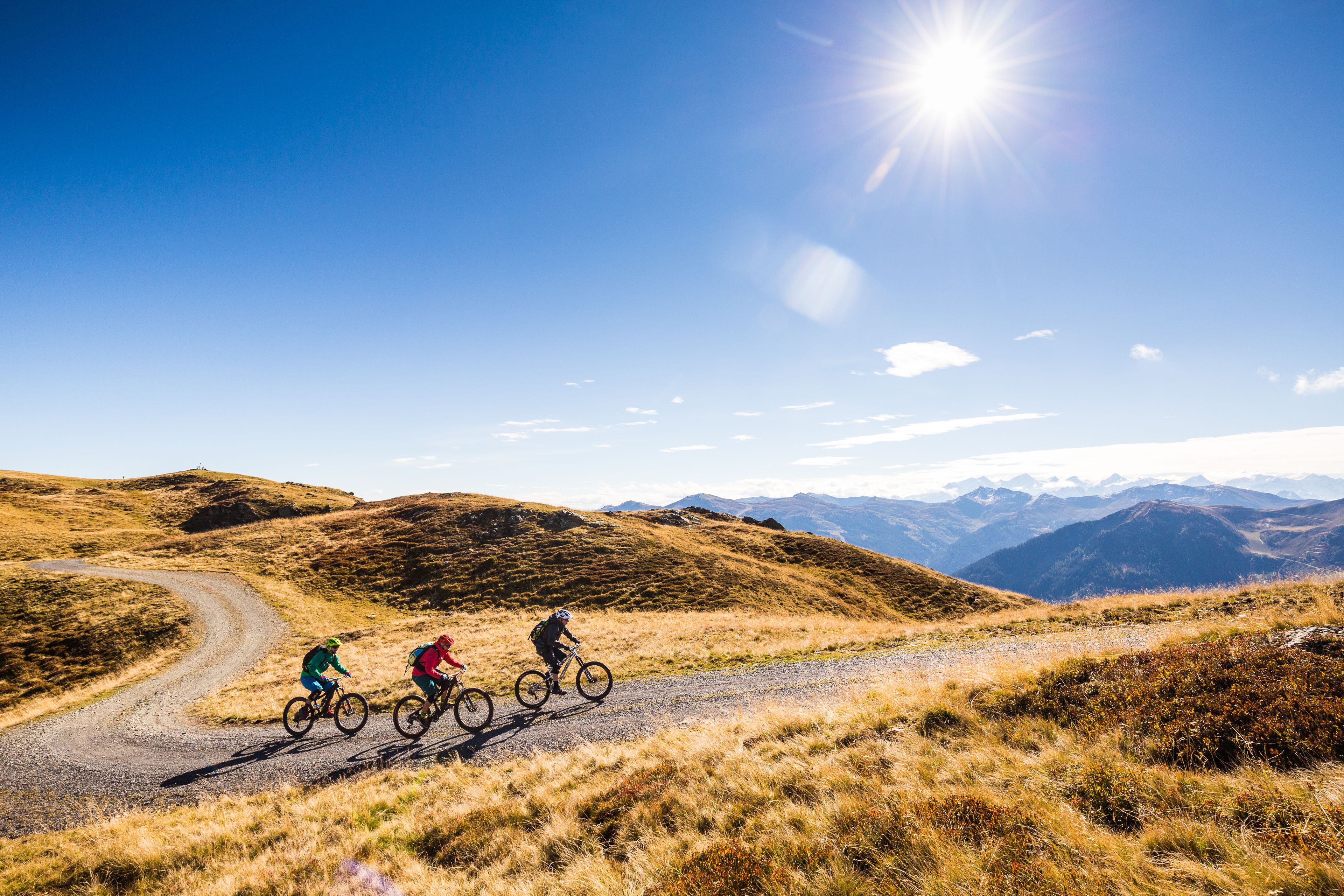 A gravel road winding through a hilly landscape with mountains in the background.