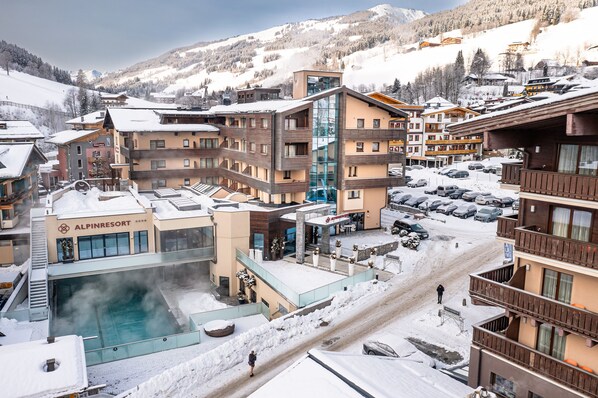 Un complejo turístico cubierto de nieve con un área de piscina, varias edificaciones y un telesilla al fondo.