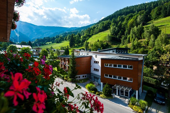 A modern building with a flat roof and large windows, surrounded by lush green hills and a clear sky.