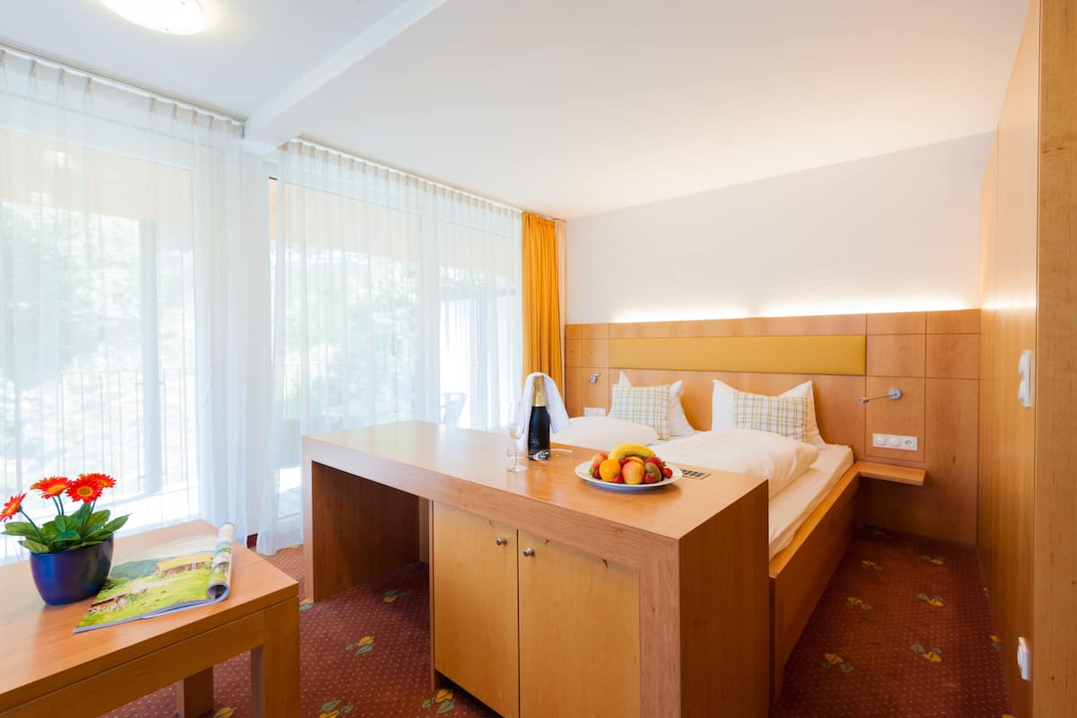 Una habitación de hotel con una cama, un escritorio, una mesita con una planta y un frutero.