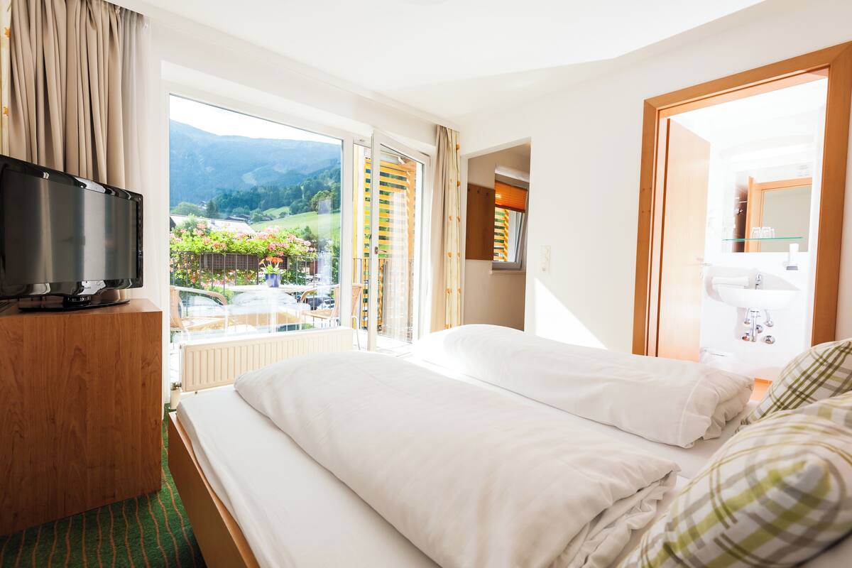 Habitación de hotel con cama, televisión, baño y balcón con vistas a las montañas.