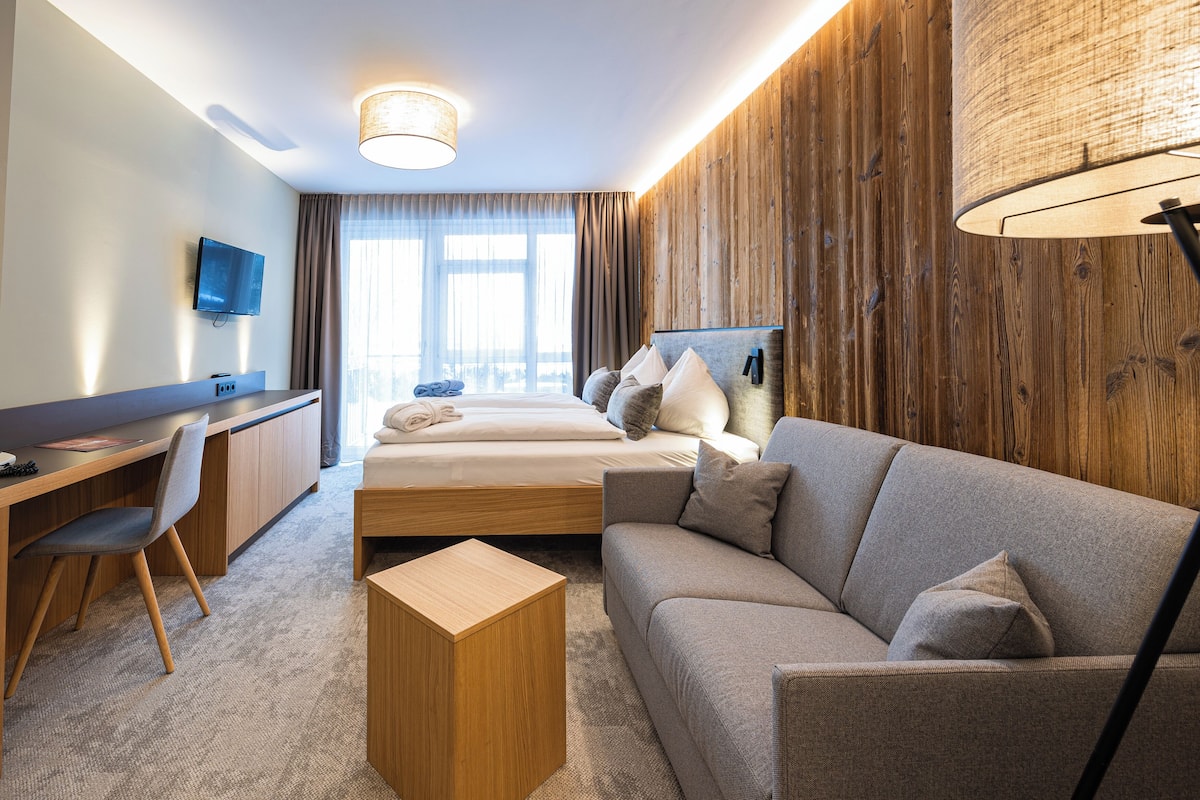 Una habitación de hotel moderna con una cama, un sofá, un escritorio y un televisor.