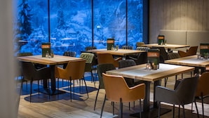 Moderni ravintola, jossa on puupöydät ja -tuolit, suuret ikkunat, joista avautuu lumisen metsänäkymä, sekä tyylikkäät menytelineet.