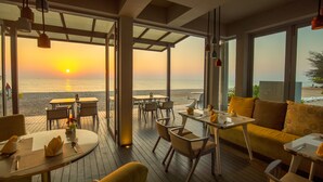 A beachside restaurant with outdoor seating, large windows, and a sunset view.