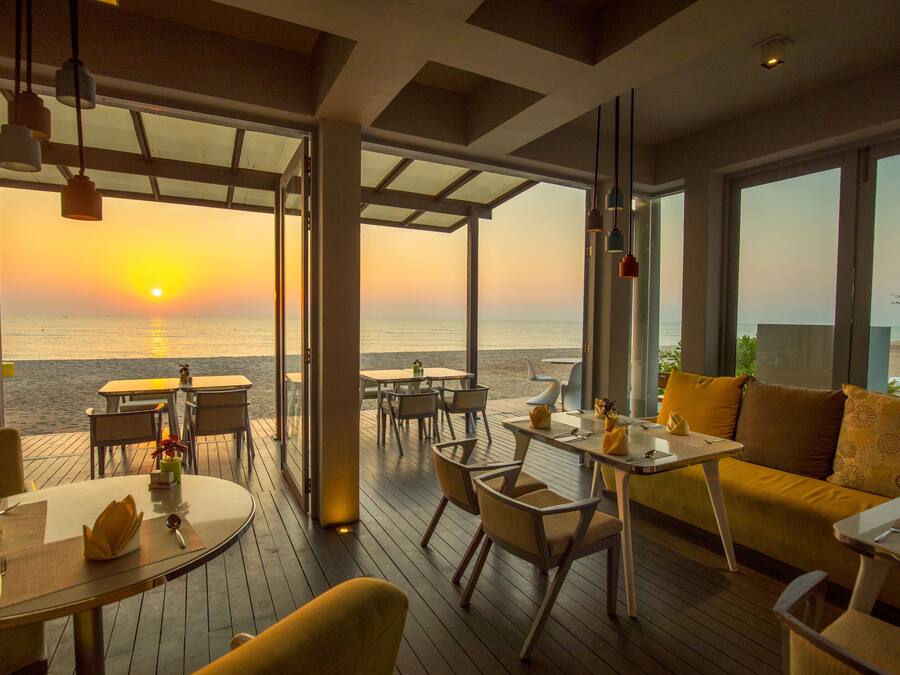 A beachside restaurant with outdoor seating, large windows, and a sunset view.