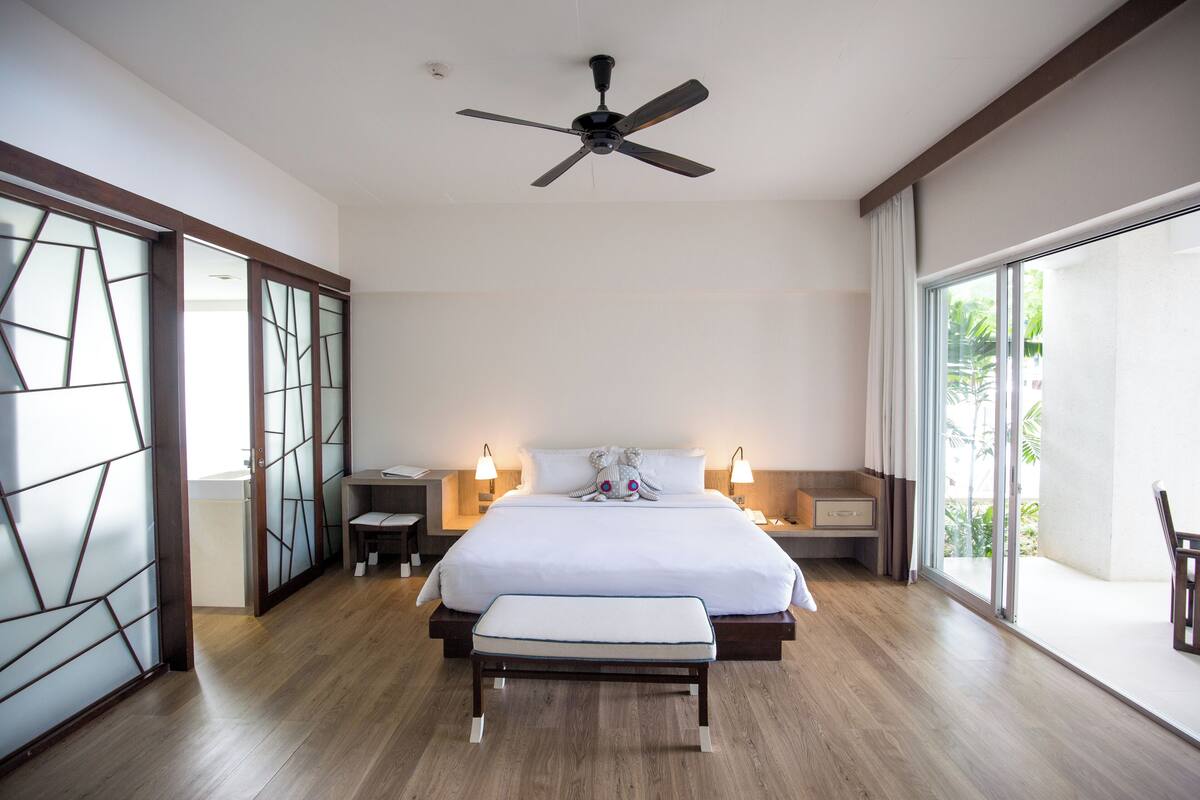 Ein modernes Schlafzimmer mit einem großen Bett, Nachttischen, einer Bank, einem Deckenventilator und Blick durch eine Glastür.