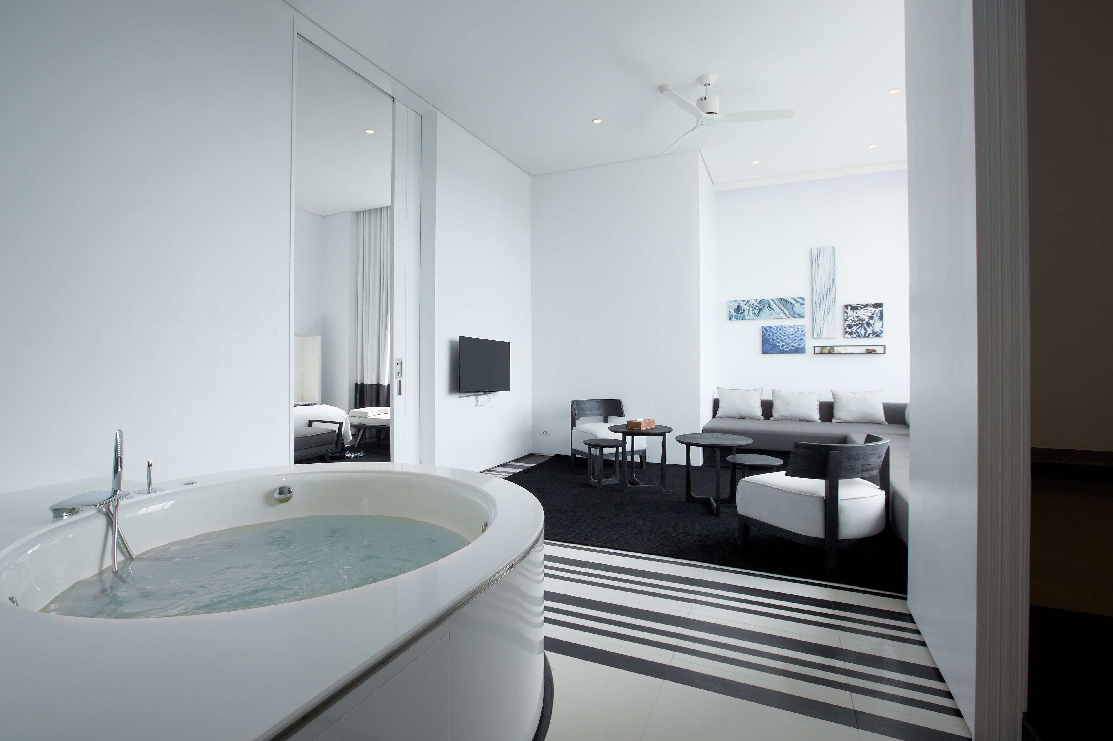 A modern bathroom with a large bathtub, a mirror, a flat-screen TV, and a seating area with a sofa and chairs.