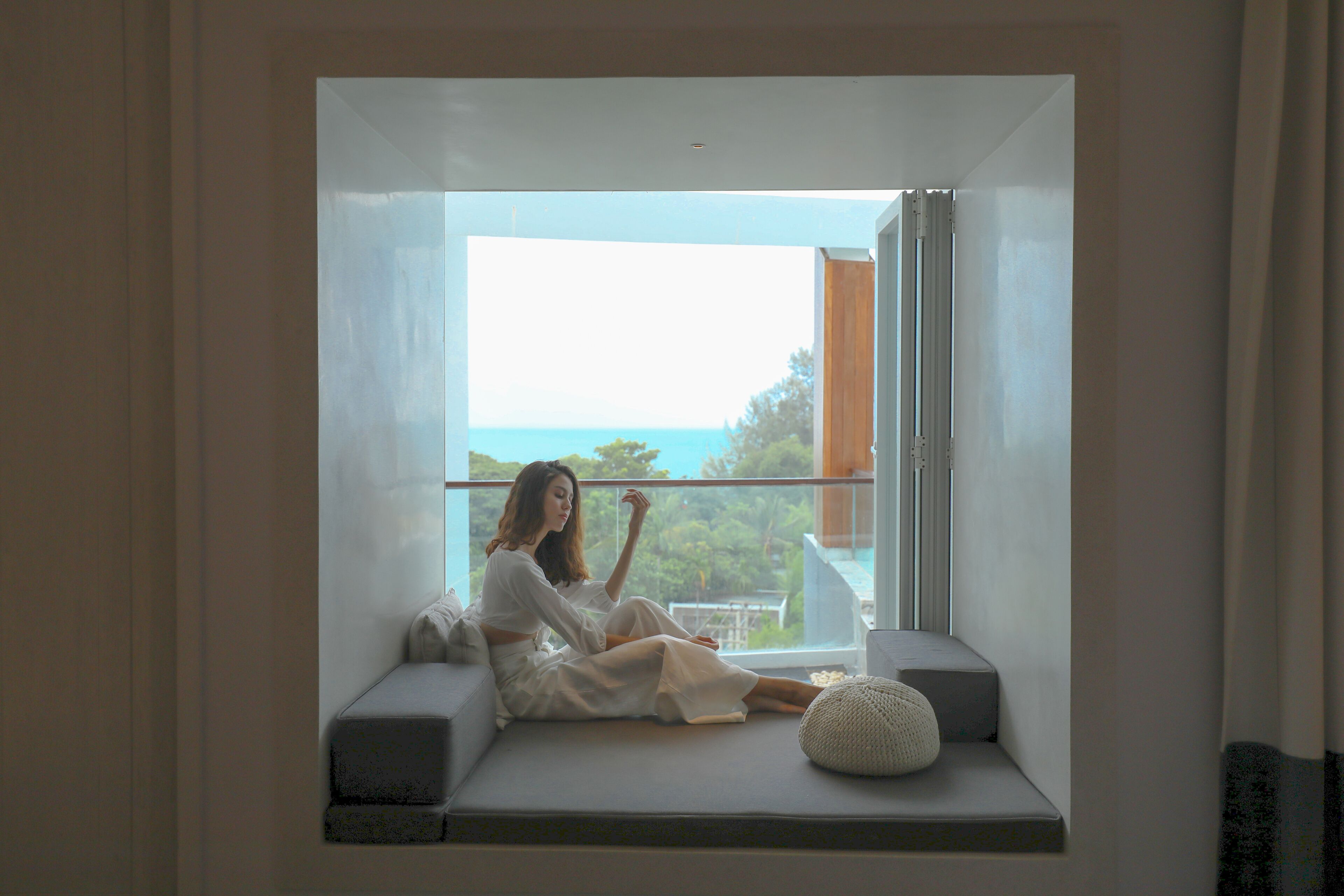 A person sitting on a window seat with a view of the sea.