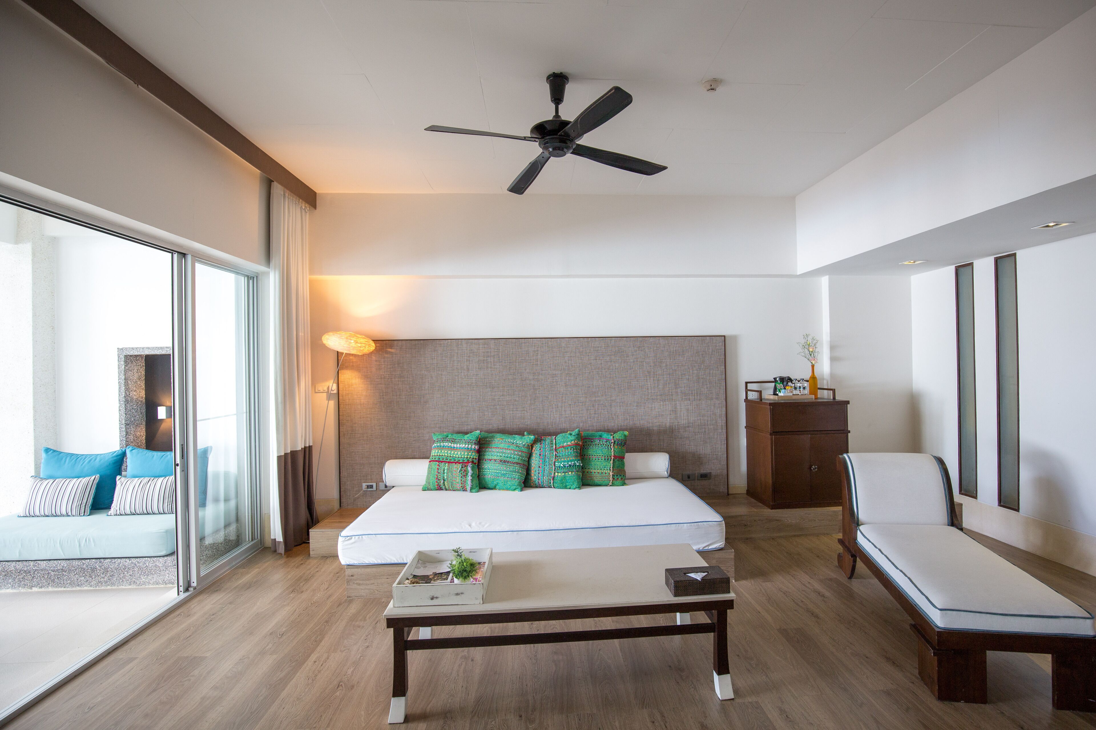 Een moderne hotelkamer met een groot bed, een plafondventilator, een nachtkastje, een stoel en uitzicht op de omgeving.