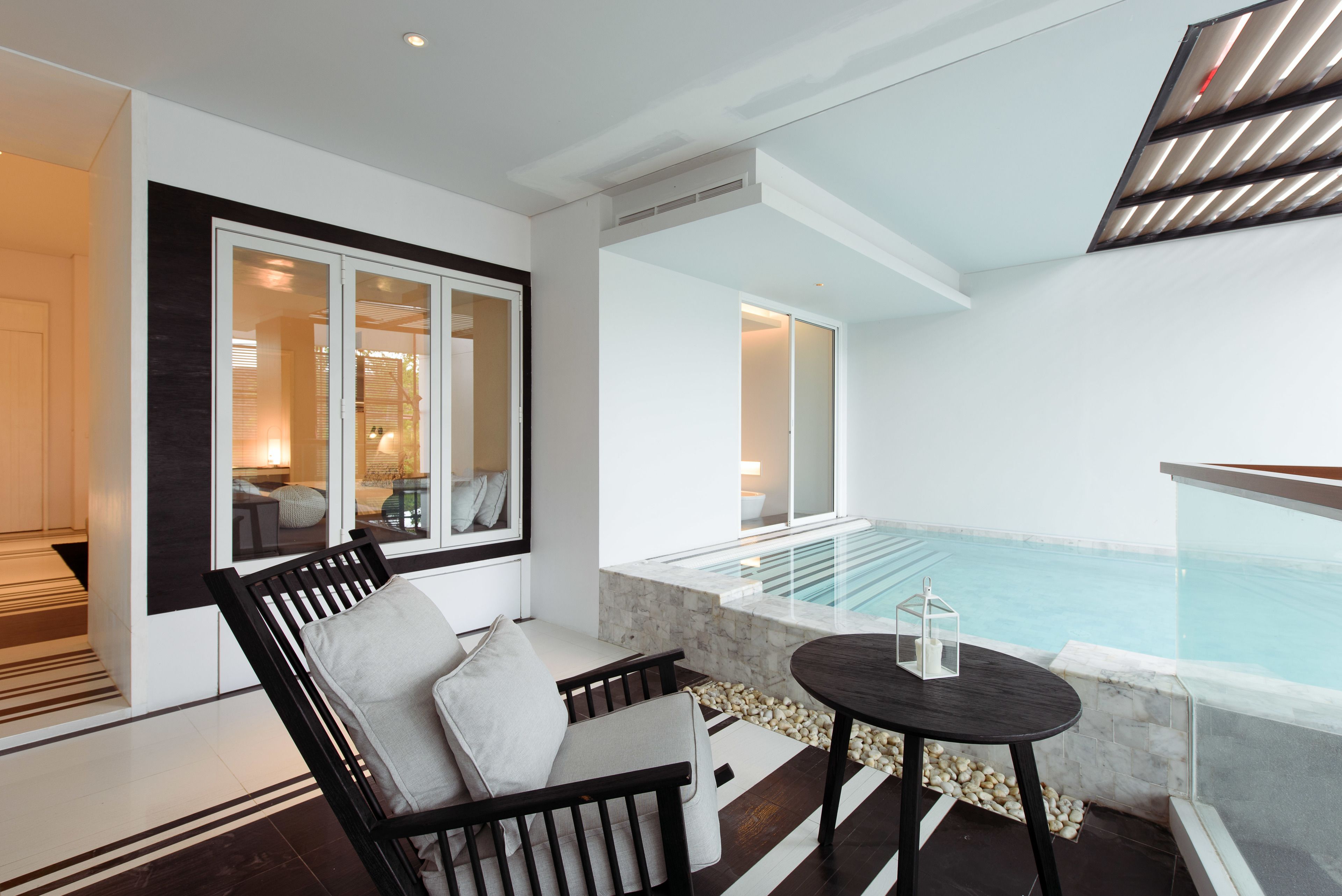 A modern indoor pool area with a glass balustrade, a seating area with a sofa and a table, and a view of the pool.