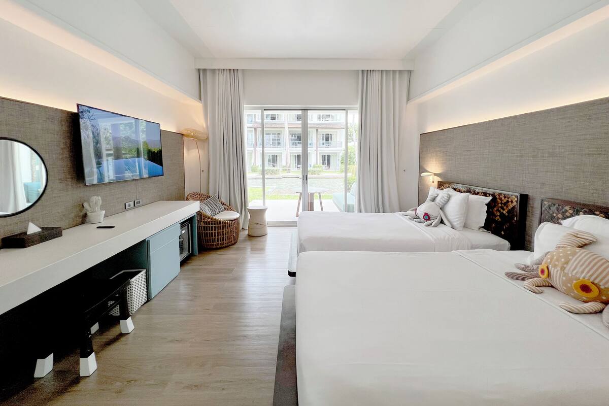 Ein modernes Hotelzimmer mit einem großen Bett, einer separaten Sitzecke, einem Schreibtisch mit Spiegel und einem Fernseher.