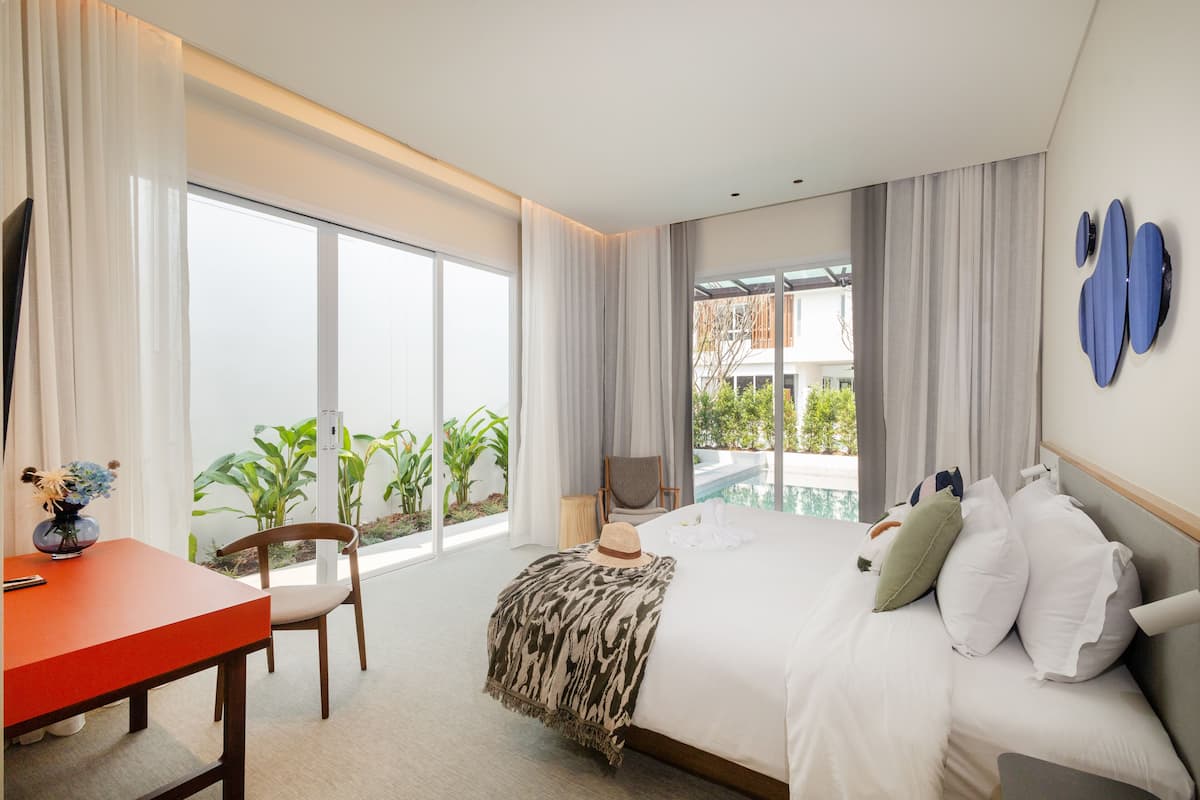 Ein Hotelzimmer mit Bett, Schreibtisch, Stuhl, Blick ins Freie und einem Pool.