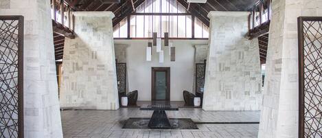 A spacious lobby with a central water feature, high ceilings with wooden beams, and stone walls.