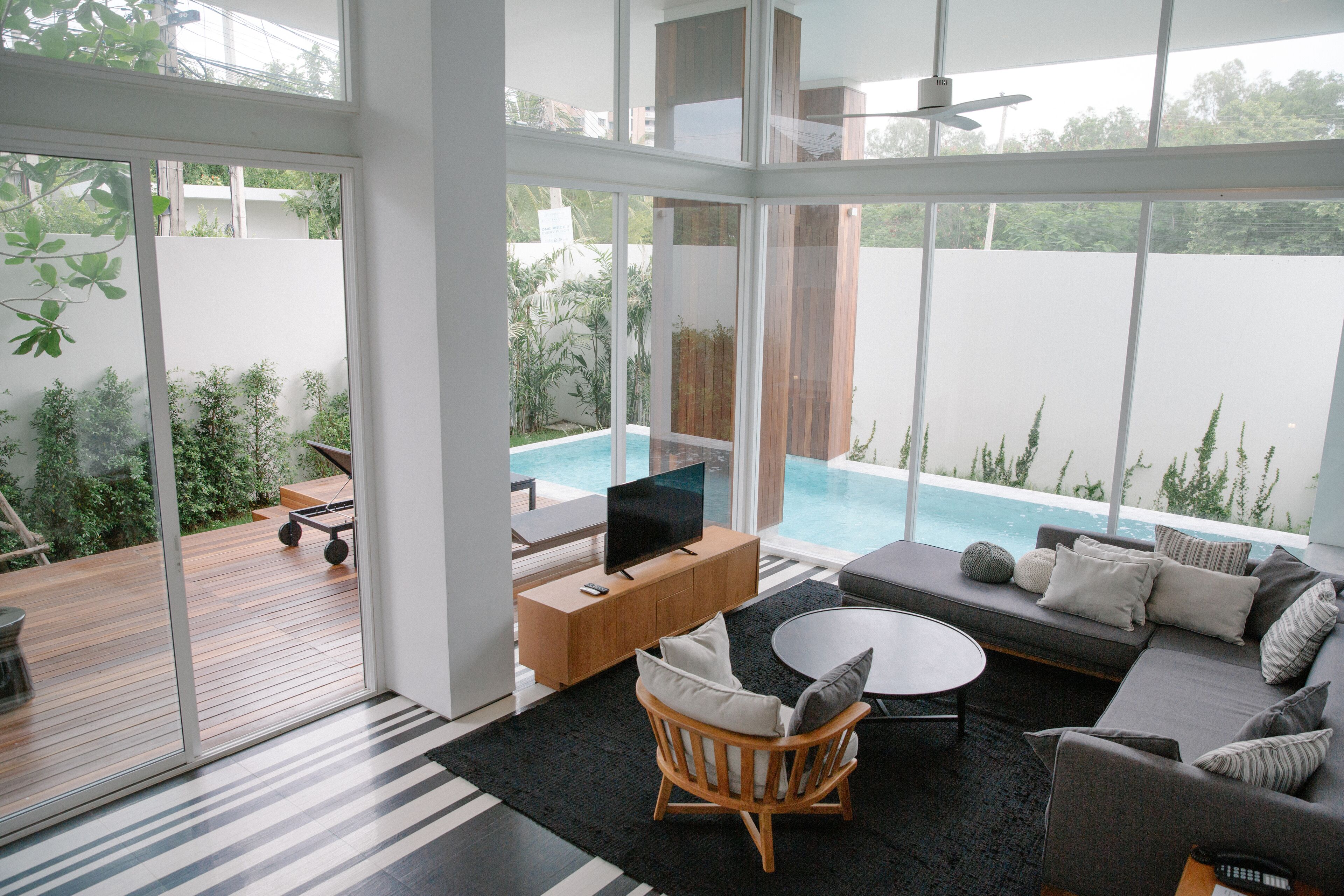 A modern living room with a pool view, a TV, and a wooden deck.
