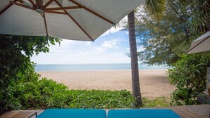 Vista de la playa desde un área cubierta con asientos, una terraza de madera y un paraguas blanco.