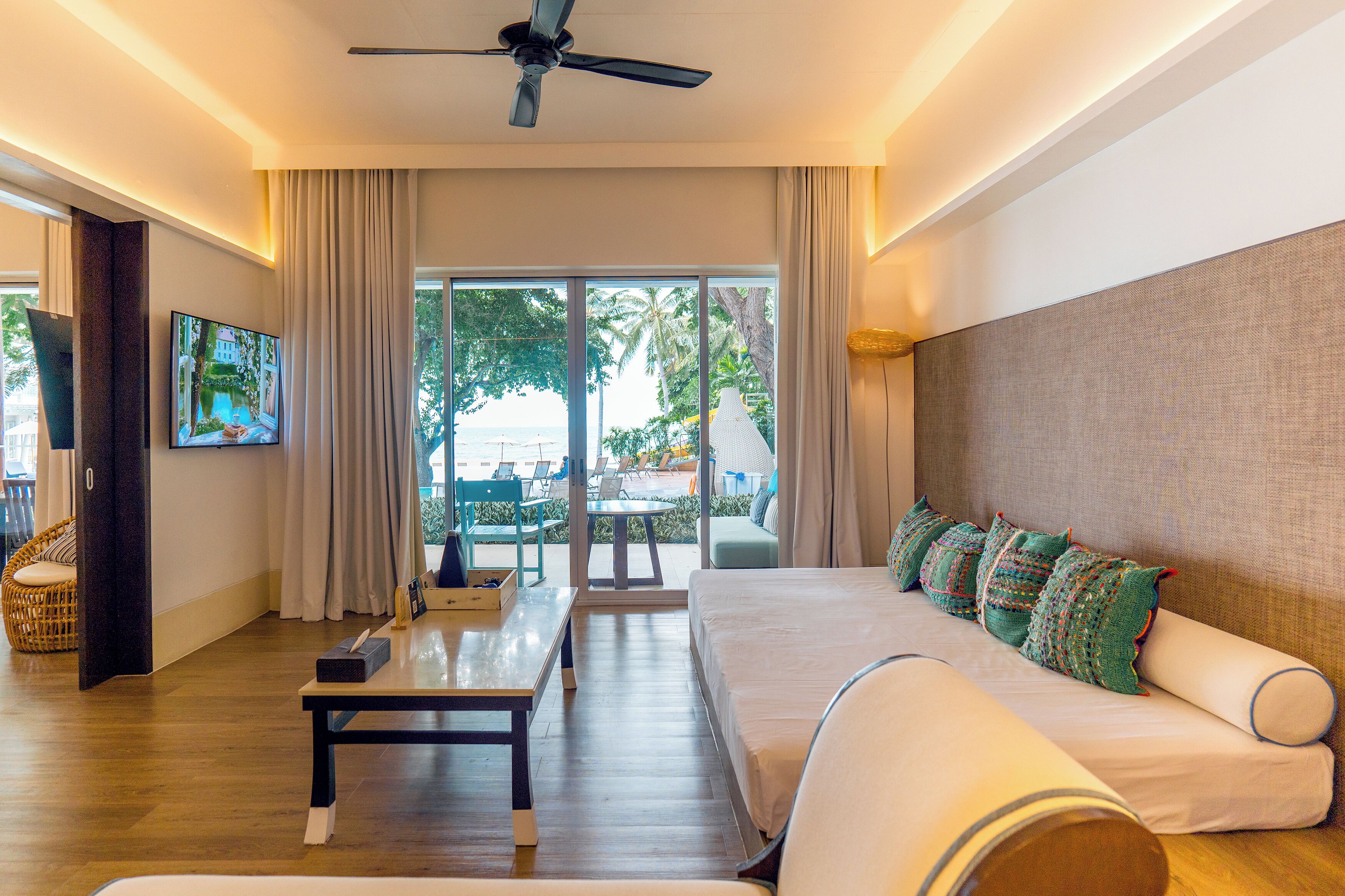 Una habitación de hotel moderna con una cama grande, un sofá, un televisor y un balcón con vistas a la playa.