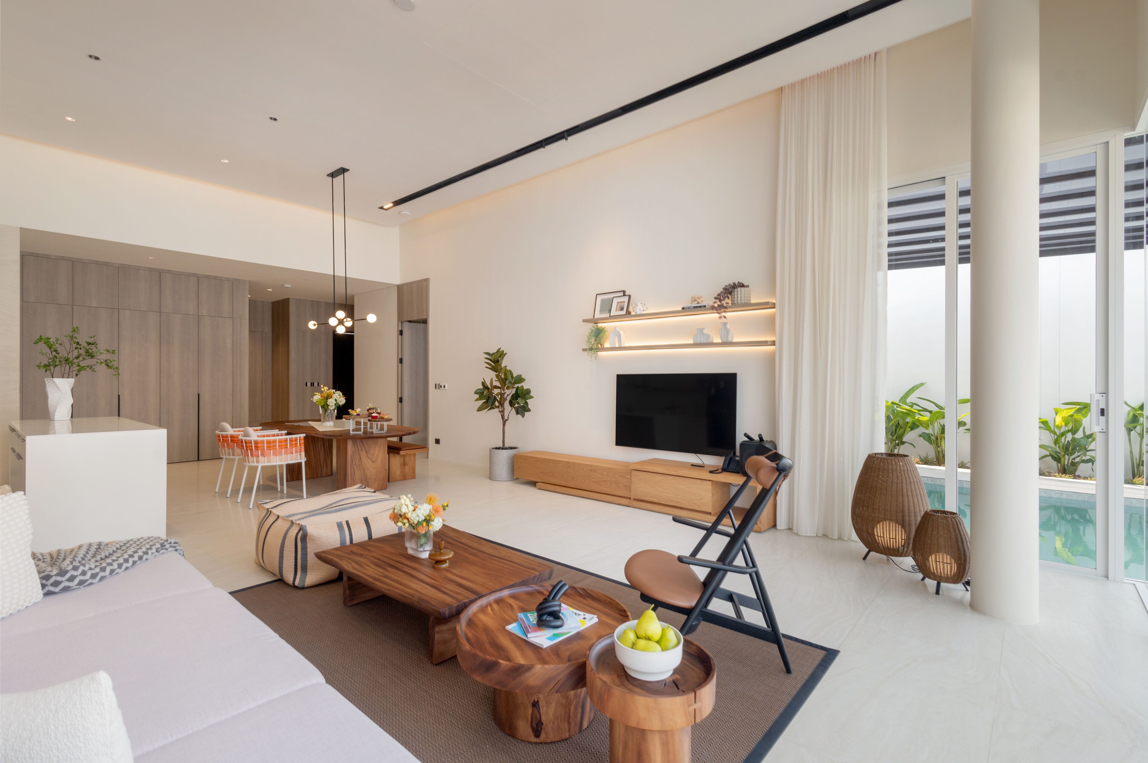 A modern living room with a sofa, coffee table, and TV. There is a dining area with a table and chairs, and a kitchen in the background.