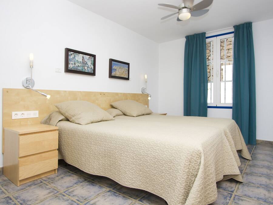 A bedroom with a bed, bedside tables, wall-mounted lamps, and a ceiling fan.