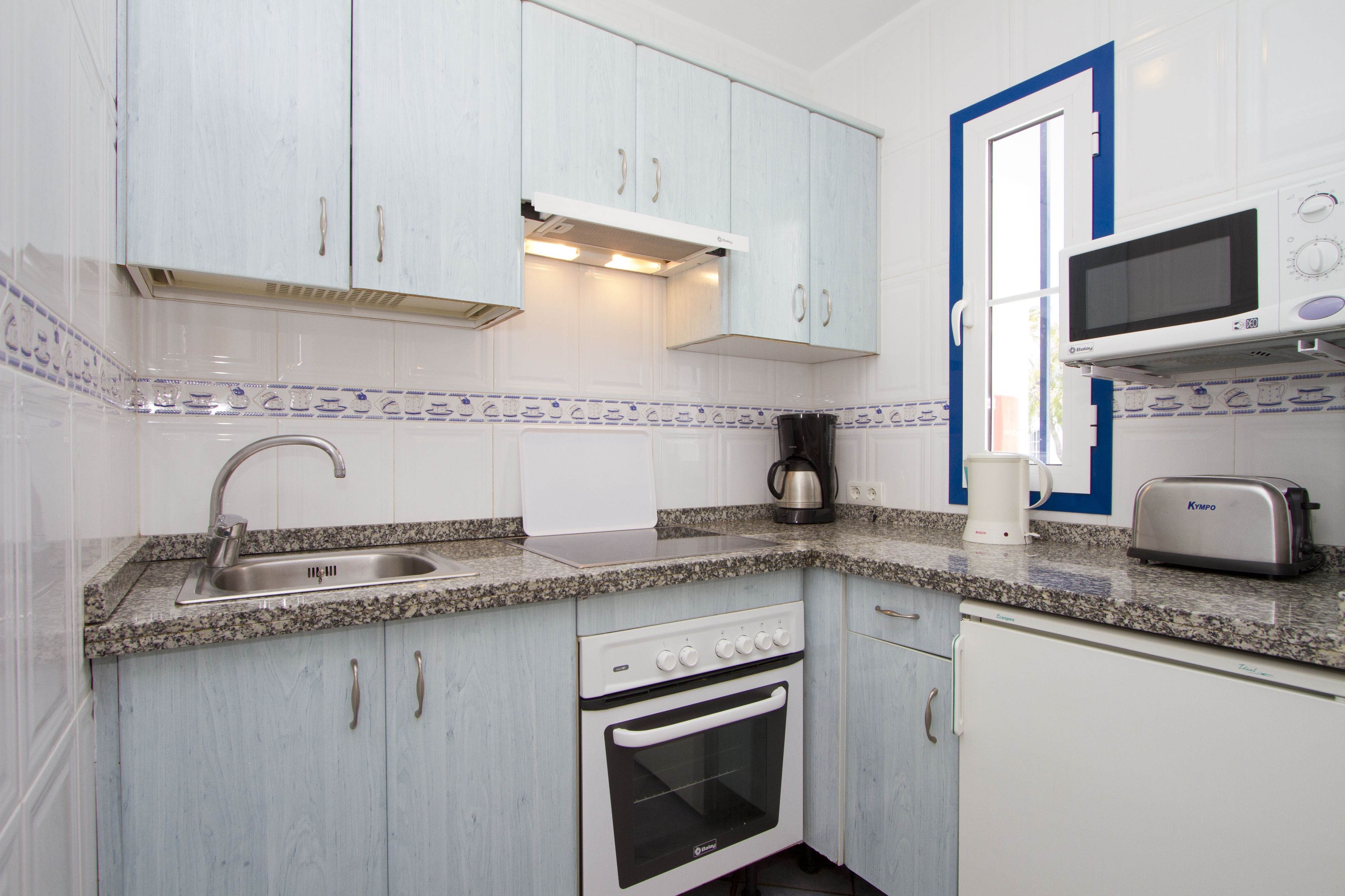 Una cocina compacta con armarios blancos, horno empotrado, microondas y cafetera.