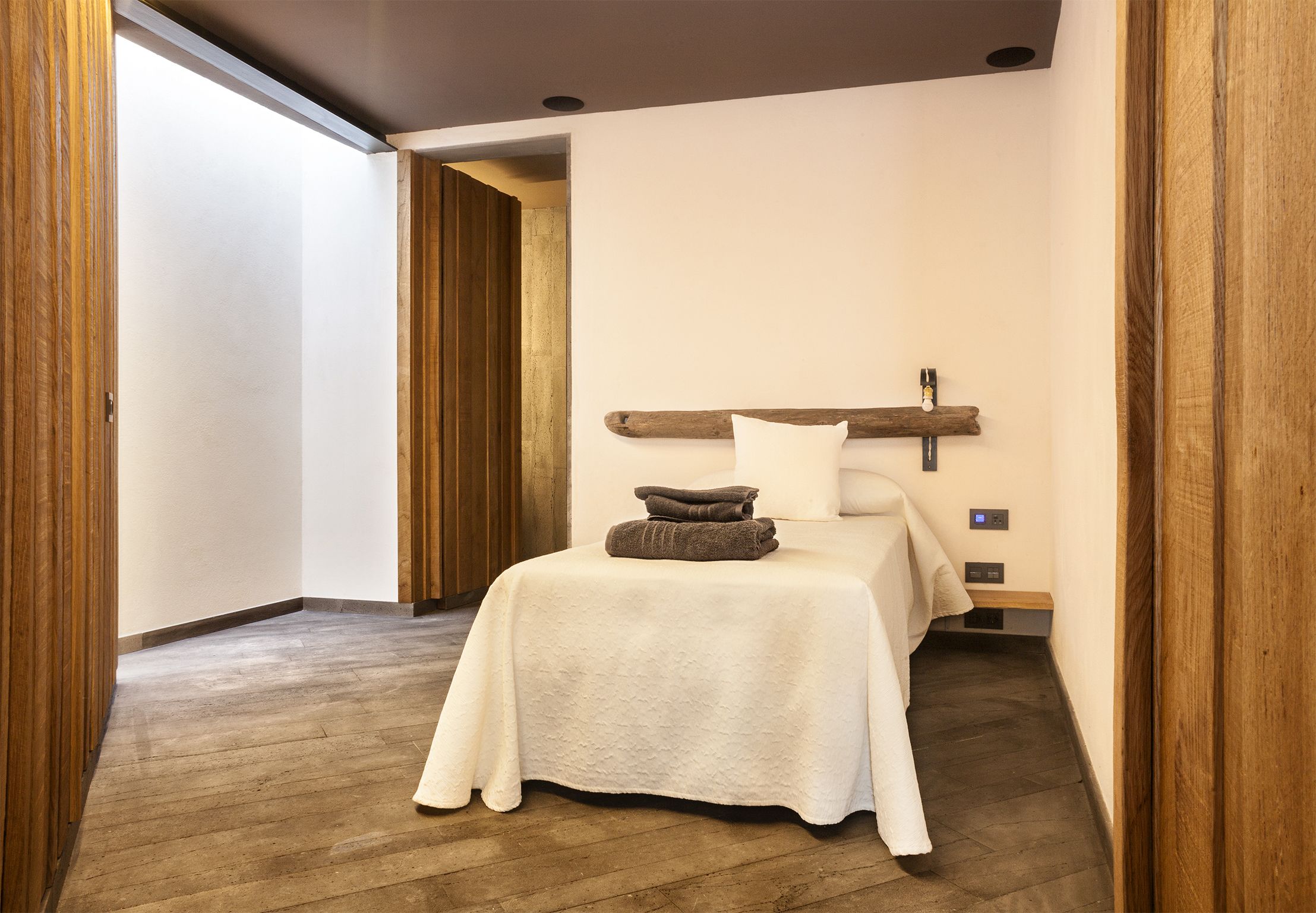 Una camera da letto moderna con pavimento in legno, un letto con copriletto bianco e una testiera in legno.
