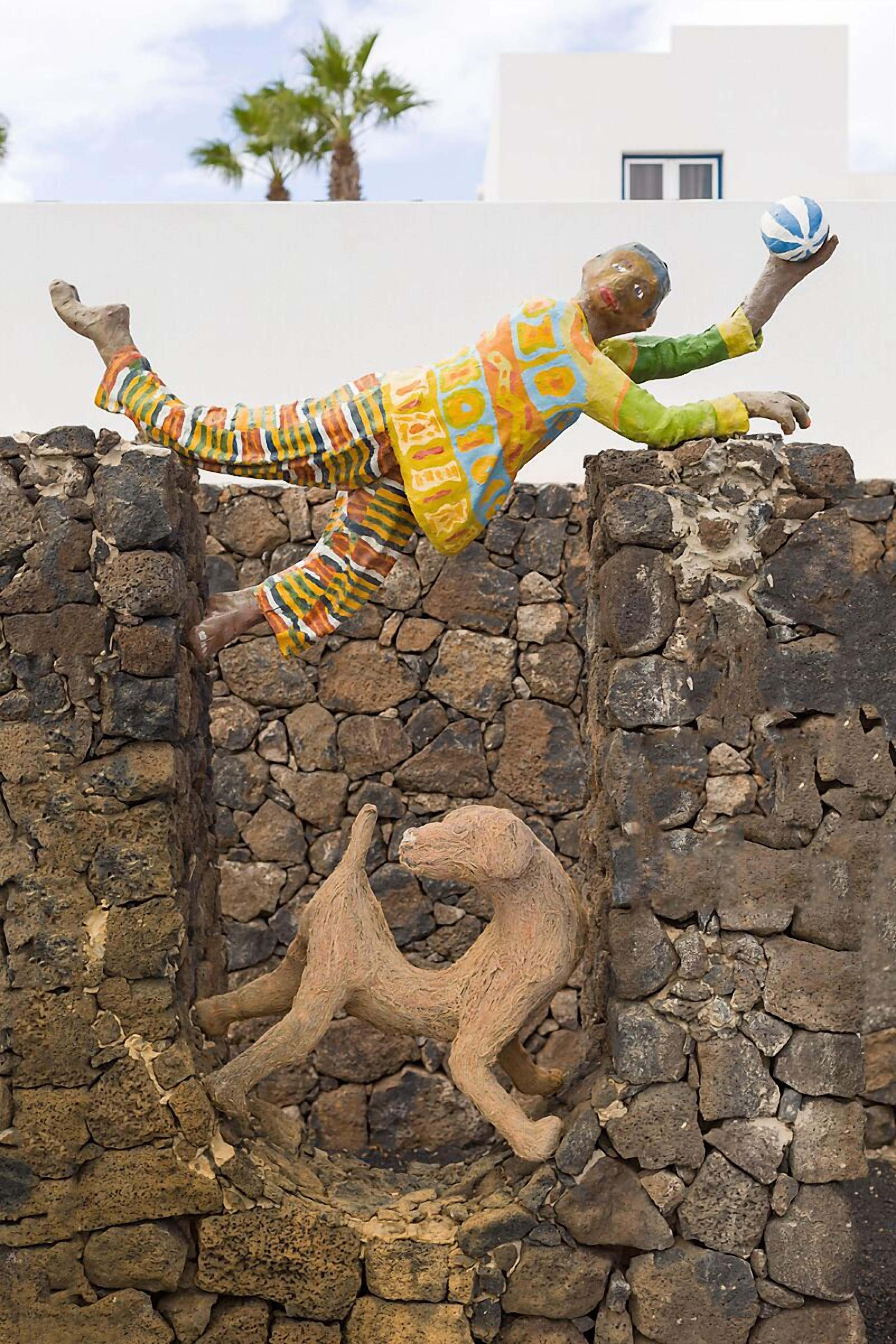 Una estatua de una persona vestida con un atuendo colorido escalando un muro de piedra.