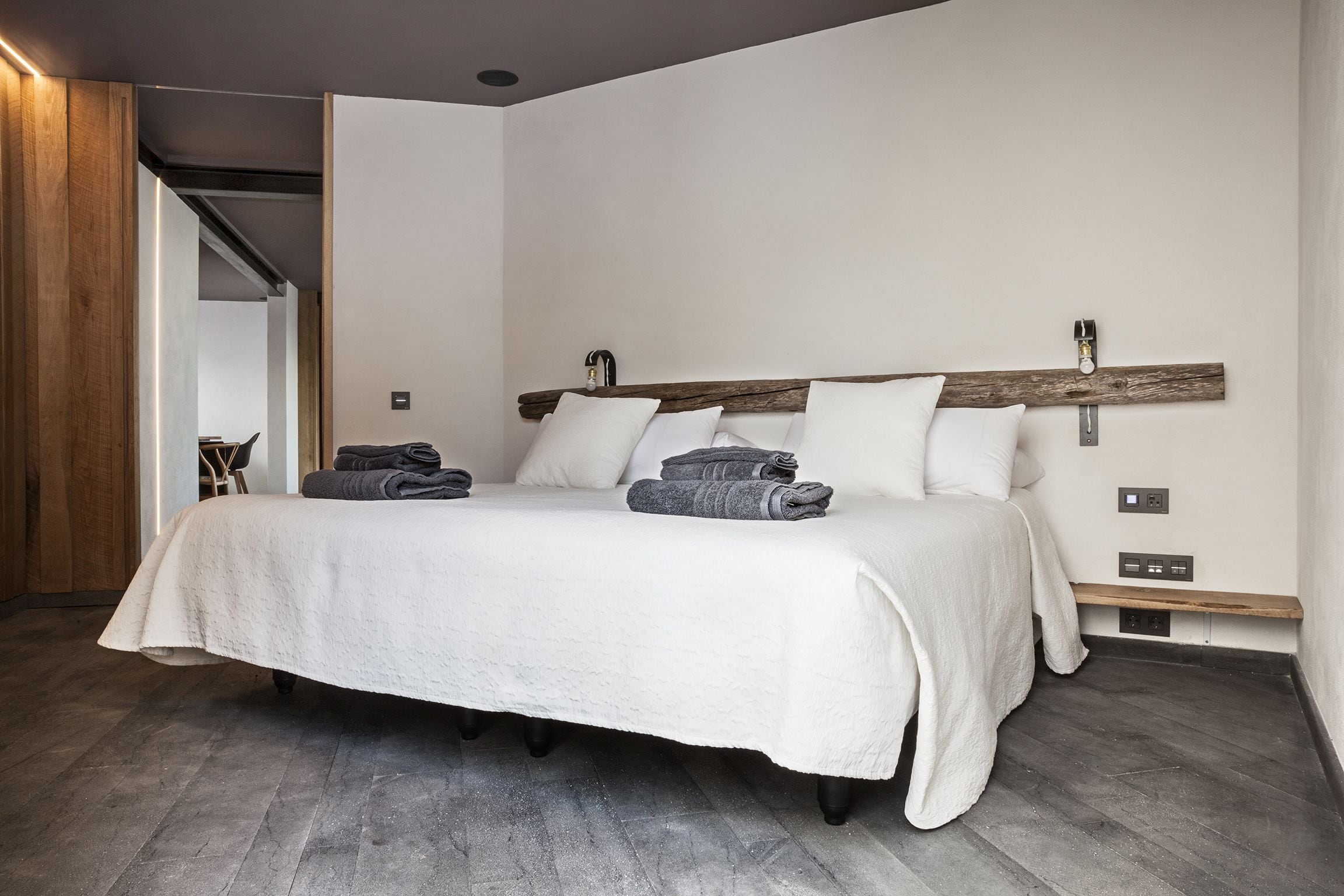 Une chambre moderne avec un grand lit, une tête de lit en bois et un banc intégré au pied du lit.