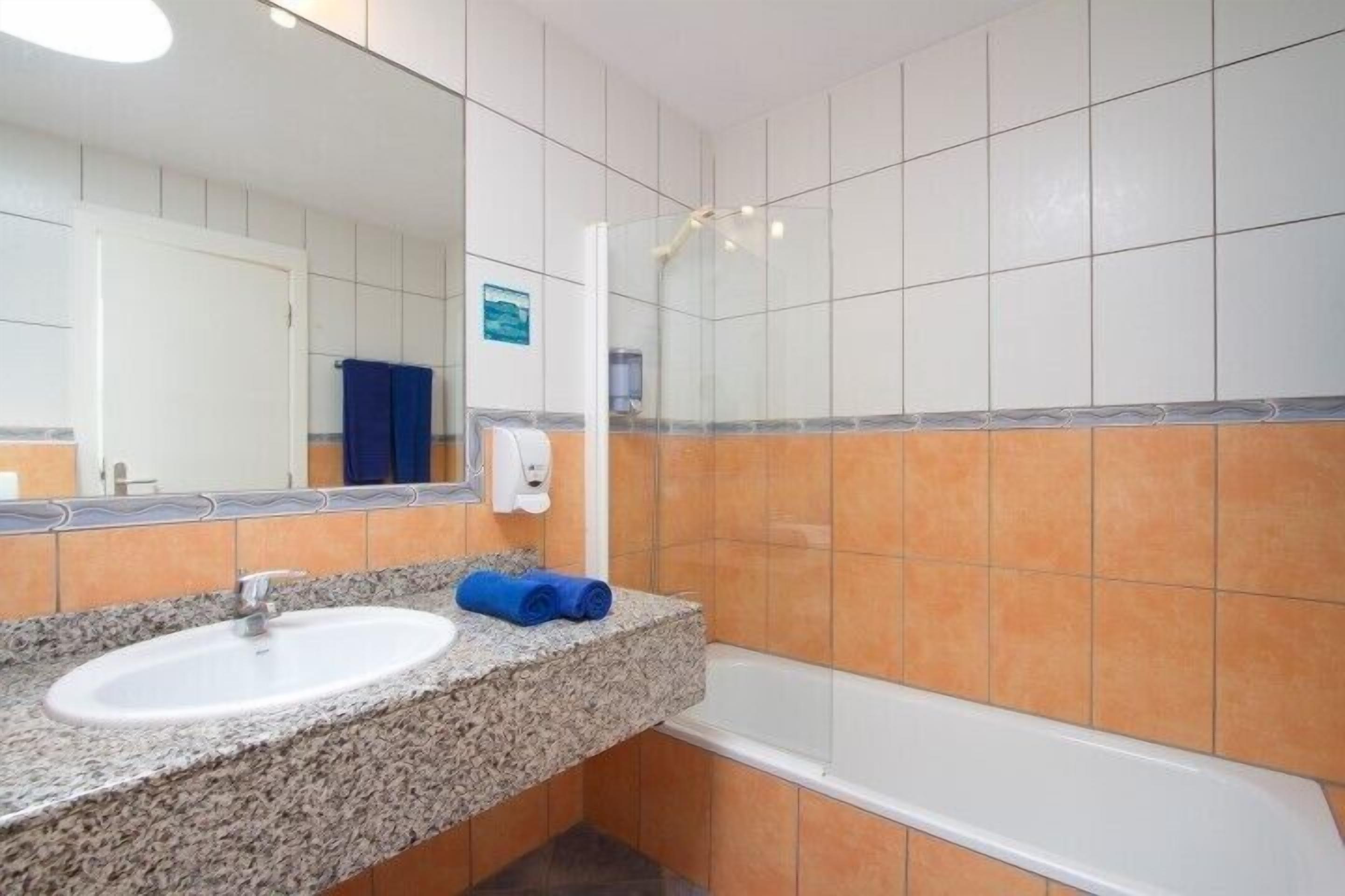 A bathroom with a granite countertop sink, a mirror, a glass shower enclosure, and orange-tiled walls.