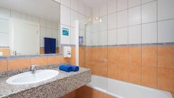 Un baño con lavamanos de encimera de granito, un espejo, cabina de ducha con mampara de vidrio y paredes de azulejos anaranjados.