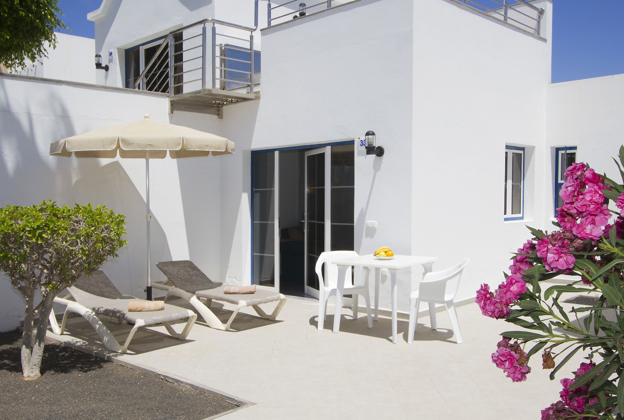 Un edificio bianco con un balcone, un tavolo con sedie, una poltrona da relax e un piccolo albero.