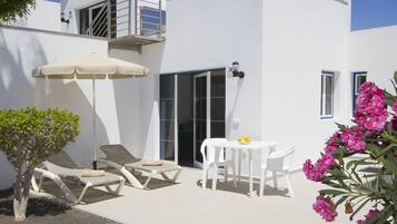 Un edificio bianco con un balcone, un tavolo con sedie, una poltrona da relax e un piccolo albero.
