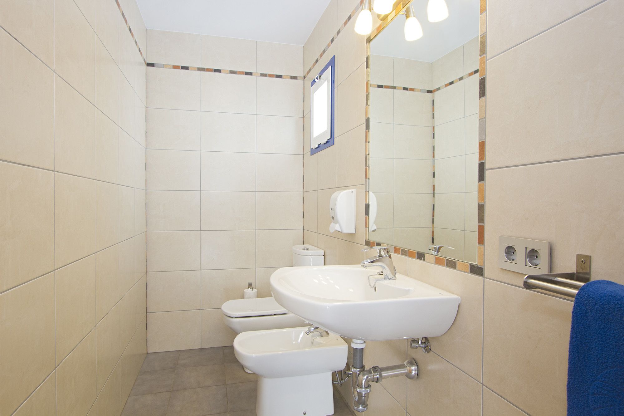 Un baño con lavamanos, inodoro, bidé y un espejo con luz.