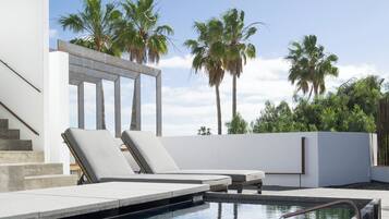 Un área de piscina moderna con sillones de descanso, vistas despejadas a palmeras y una escalera que conduce a un nivel superior.