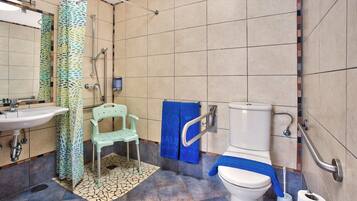 A bathroom with a sink, toilet, shower, and a chair.