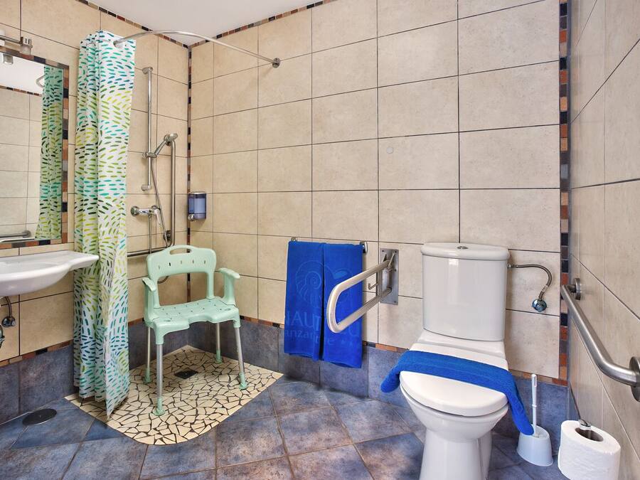 A bathroom with a sink, toilet, shower, and a chair.