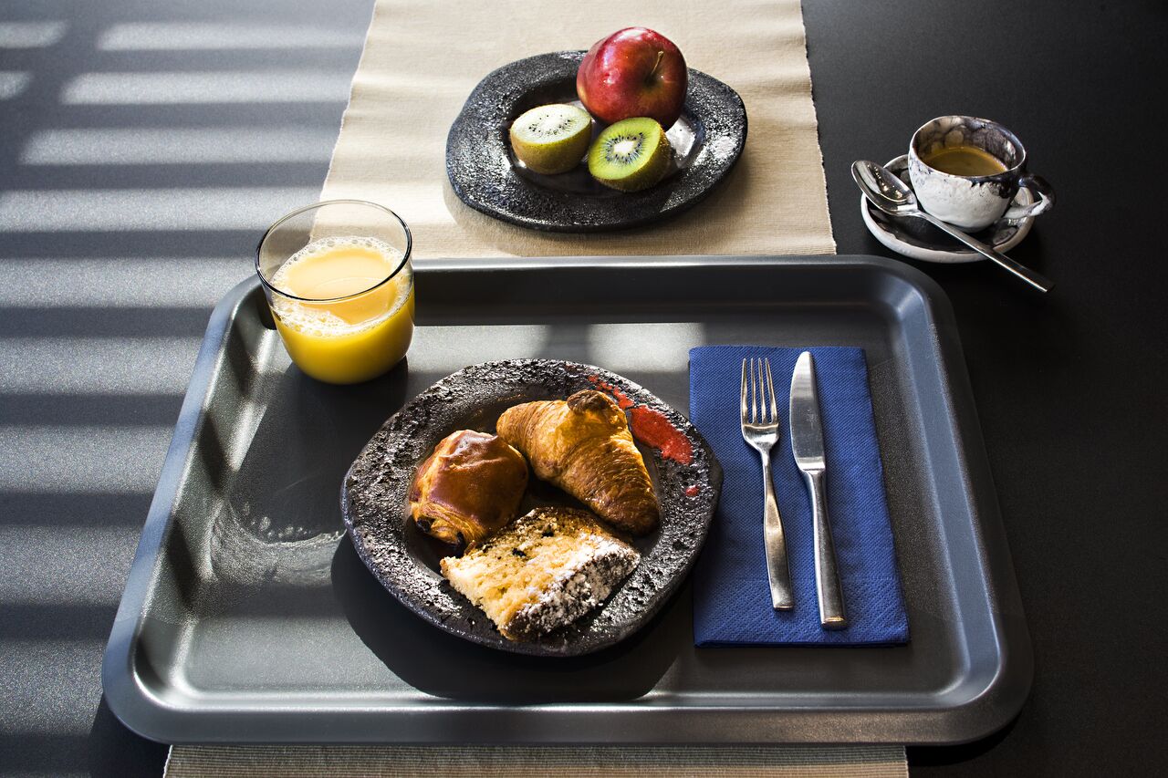 A breakfast tray with croissants, a slice of cake, and a glass of orange juice.