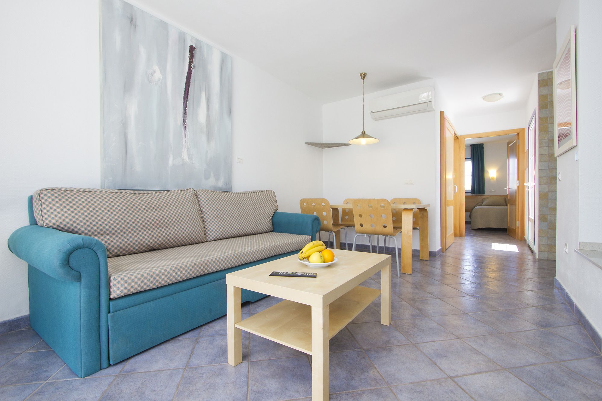 Een moderne woonkamer met een blauwe bank, een houten salontafel met fruit, en een eethoek met stoelen en een tafel.
