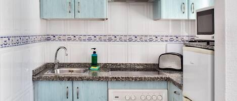 A compact kitchen with teal cabinets, a built-in oven, a microwave, and a toaster.