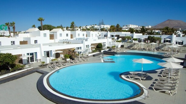 Un resort con una piscina grande, edificios blancos y una montaña al fondo.