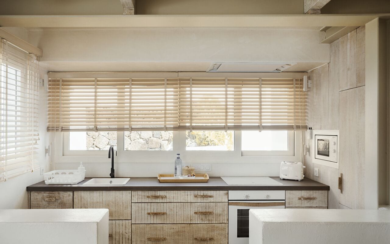 Una cocina moderna con un ventanal grande, armarios de madera y encimera blanca.