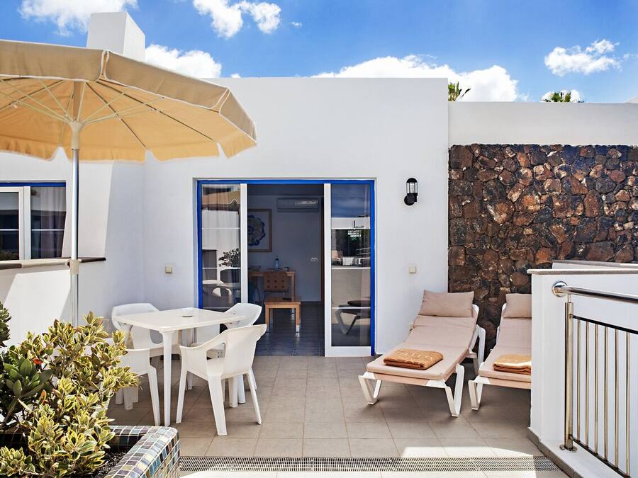 Een terras met een tafel, stoelen en een lounge stoel, en een stenen muur.