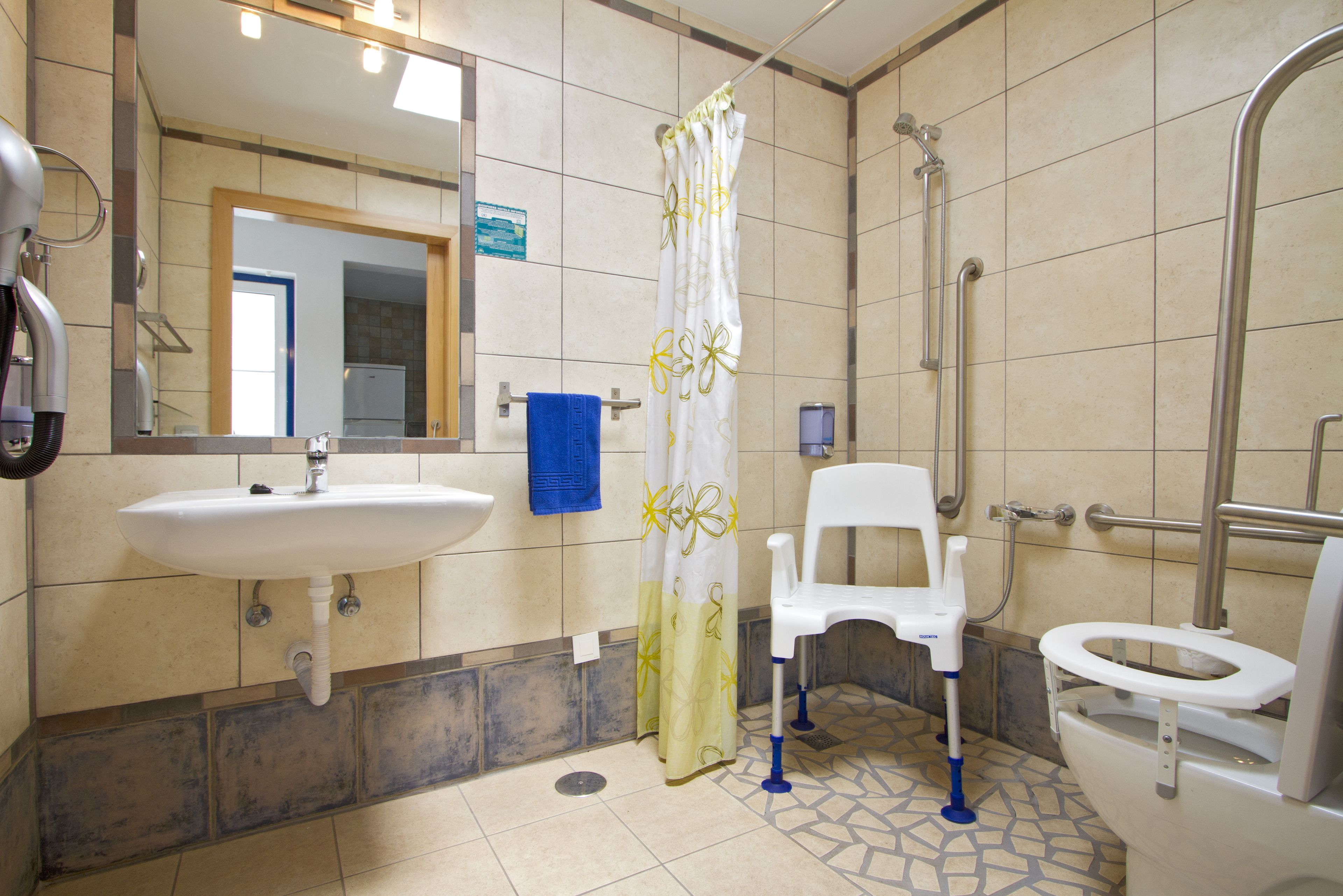 A bathroom with a sink, toilet, shower, and a wheelchair-accessible chair.
