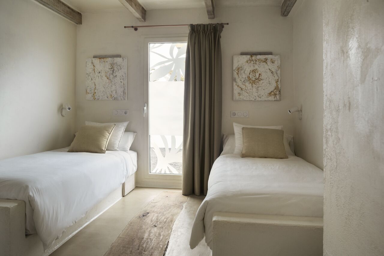A room with two beds, a window with curtains, and two abstract paintings on the walls.