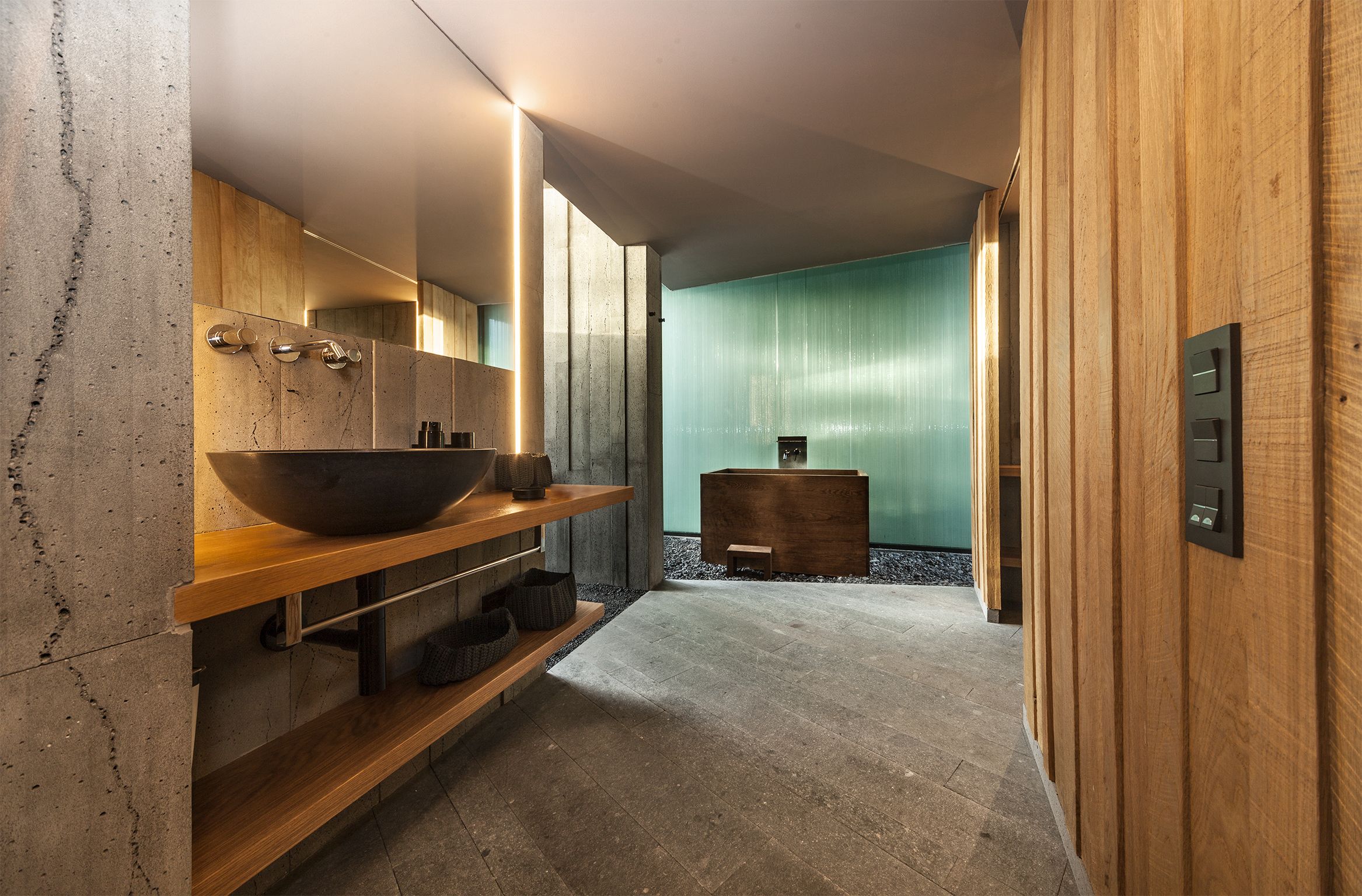Un baño moderno con un lavabo grande, estantes de madera y suelo de piedra.
