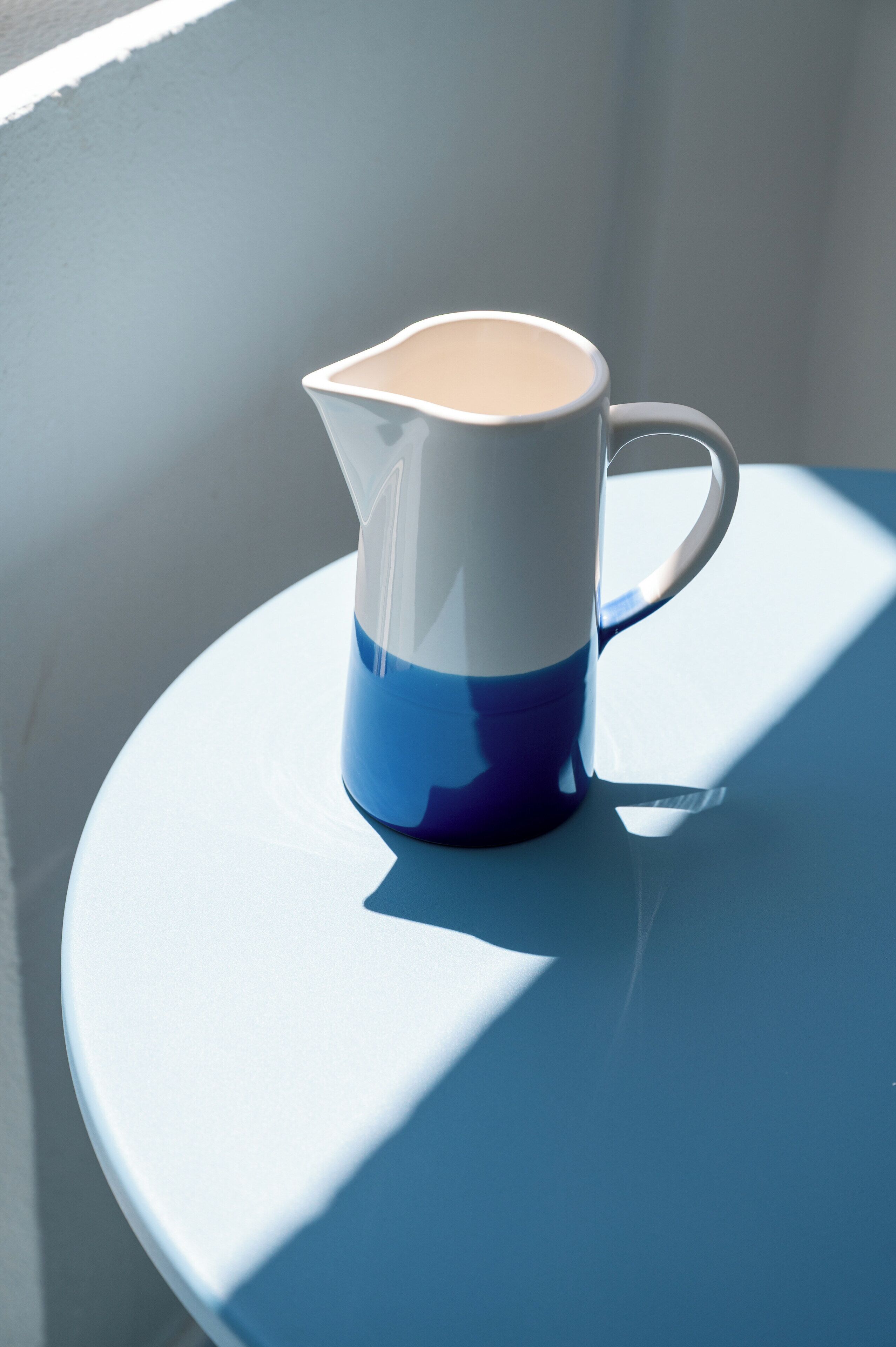 A white and blue pitcher on a round table with a shadow cast on it.