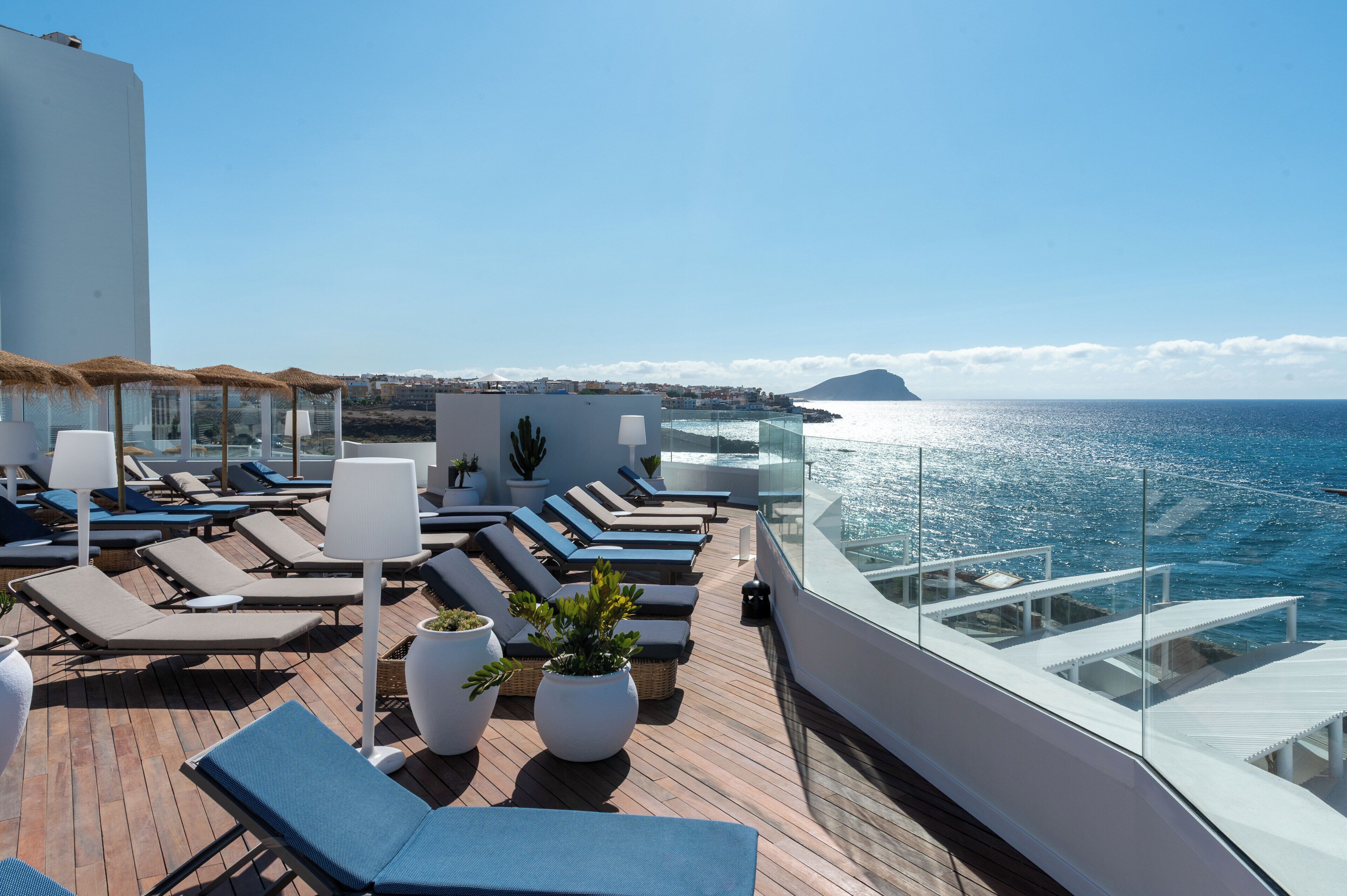 Terraço com espreguiçadeiras e plantas em vasos, com vista para a costa.