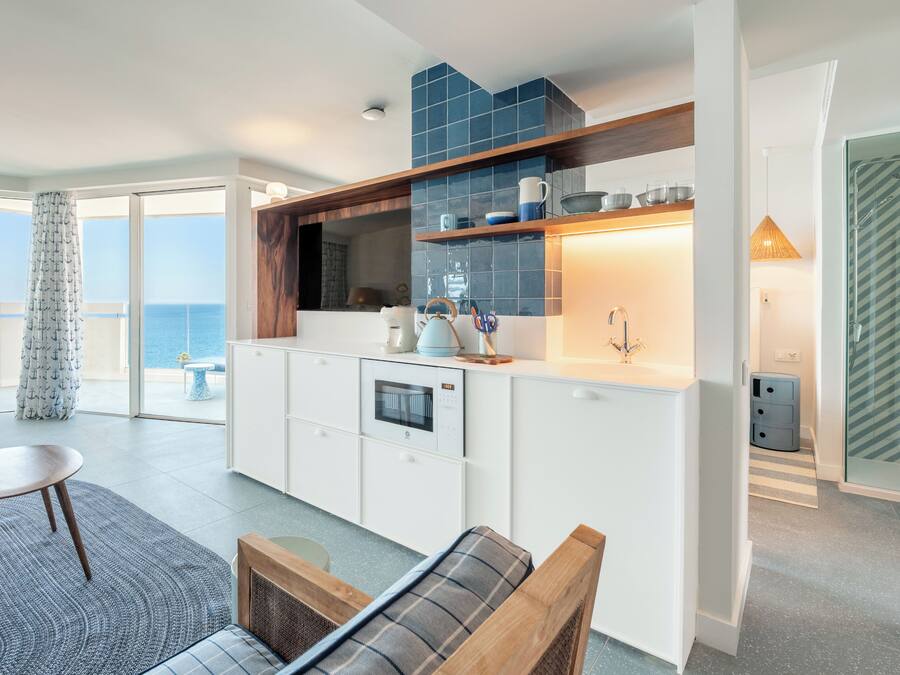 Cocina moderna con vista al mar, comedor con mesa y banco, y ducha con cerramiento de vidrio.