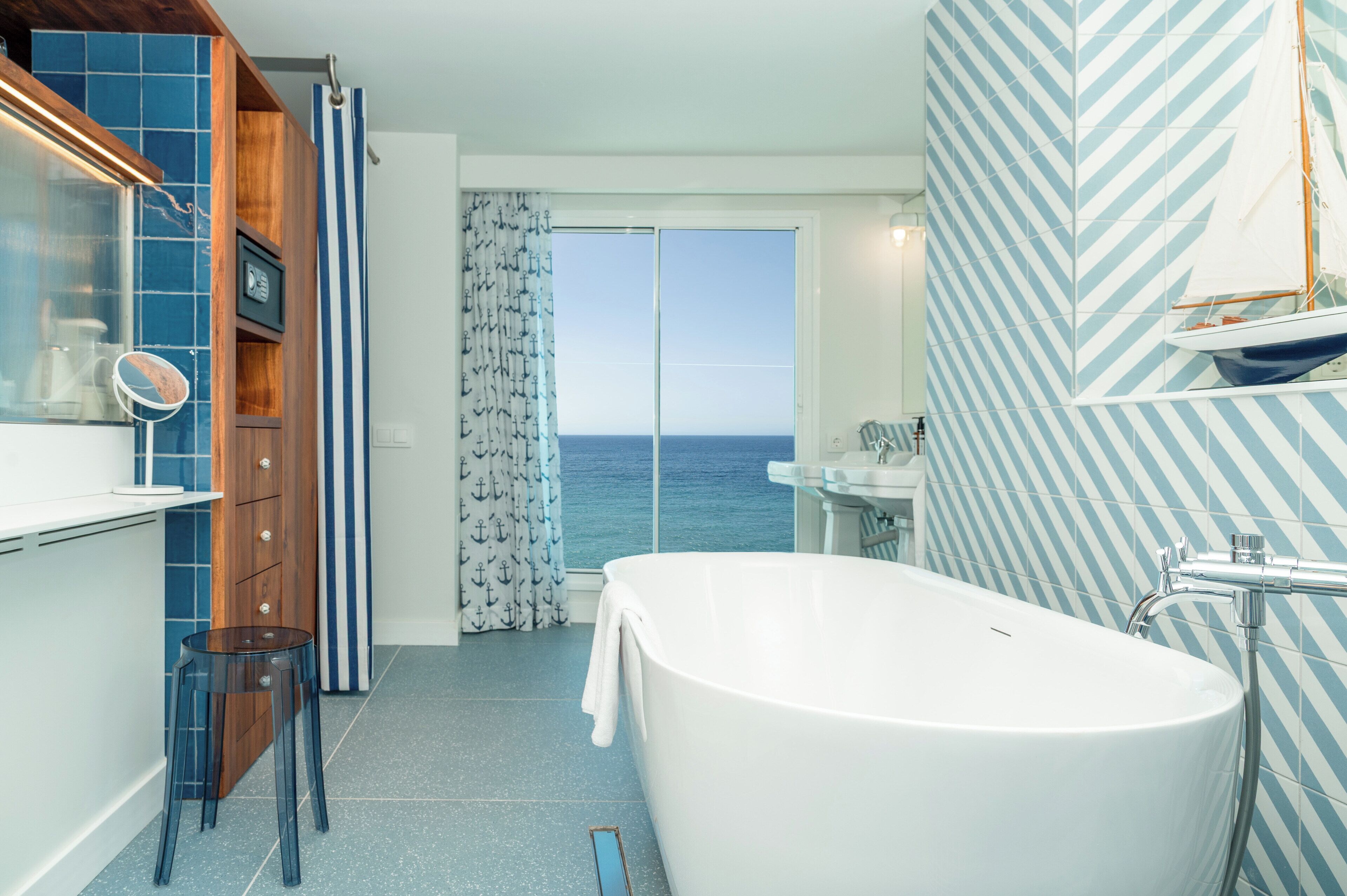 A bathroom with a large bathtub, a mirror, and a view of the sea through a glass door.