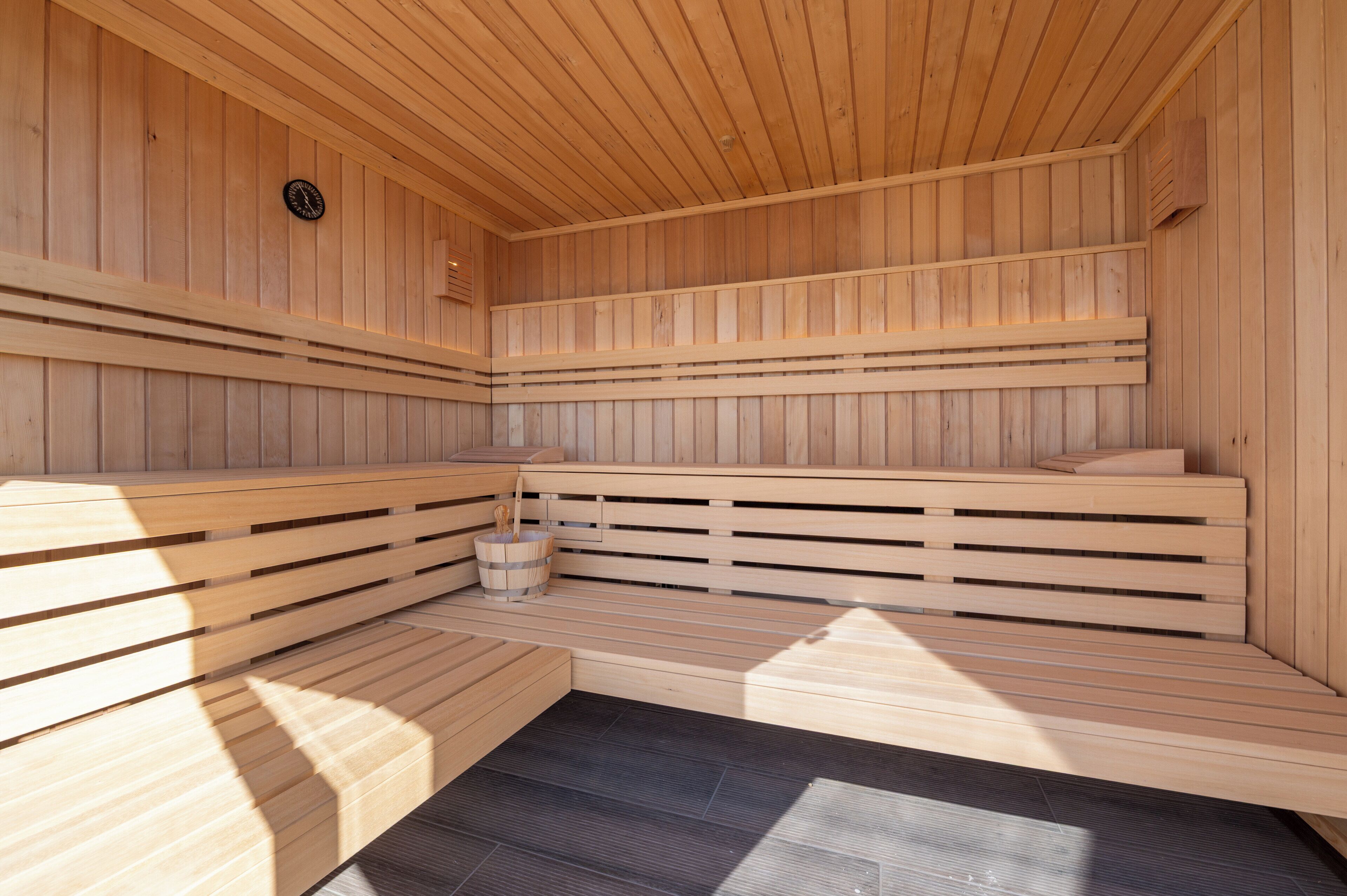 Una sauna con bancos de madera y un cubo pequeño.